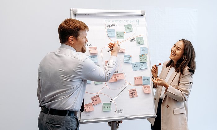 A man and a woman are standing in front of a flipchart with lots of post-it notes and discussing them.