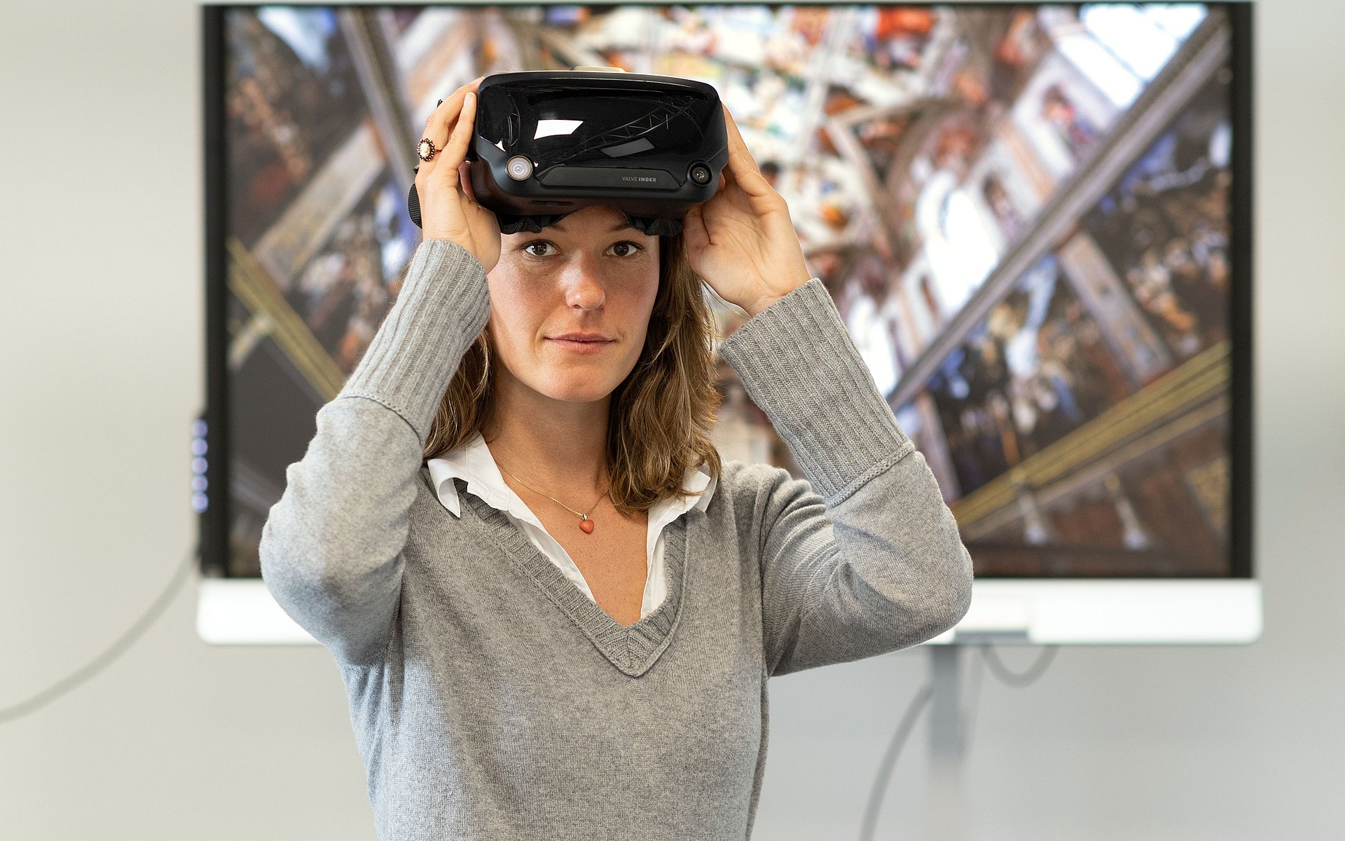 Eine Frau mit einer VR-Brille steht vor einem Bildschirm. 