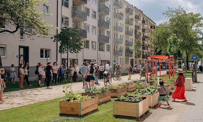 Menschen treffen sich in einem Münchner Straßenzug, der durch Pflanzenkästen begrünt wurde