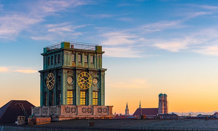 Die Skyline der Münchner Innenstadt bei Sonnenuntergang. Im Fokus steht der Thiersch-Turm, ein Glockenturm und das Wahrzeichen der TUM.