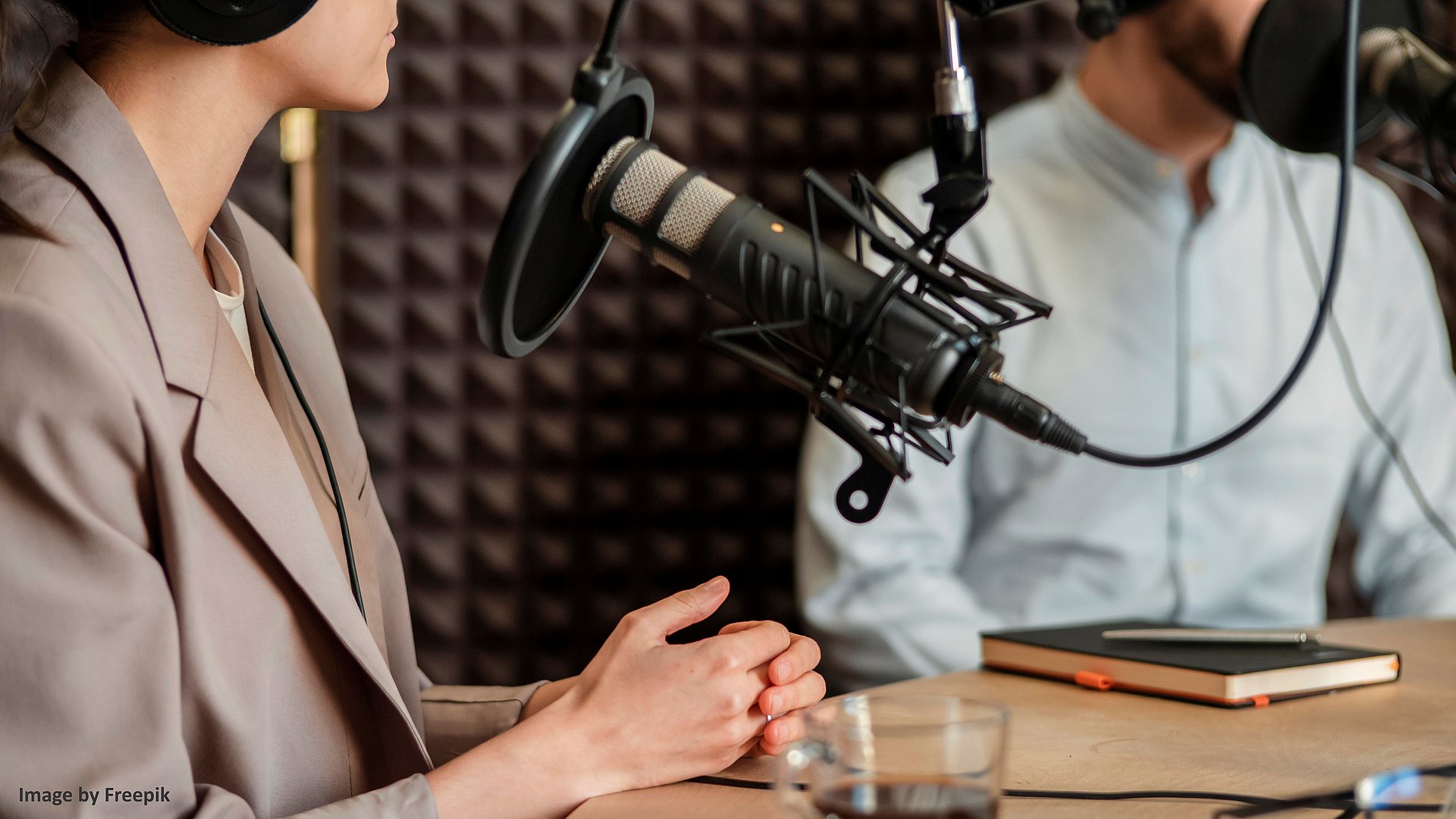 Eine Frau und ein Mann sitzen in einem Aufnahmestudio und nehmen einen Podcast auf. 
