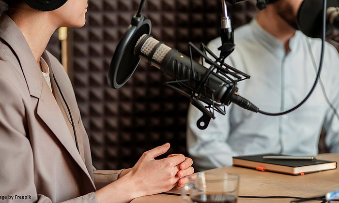 A woman and a man sit in a recording studio and record a podcast.