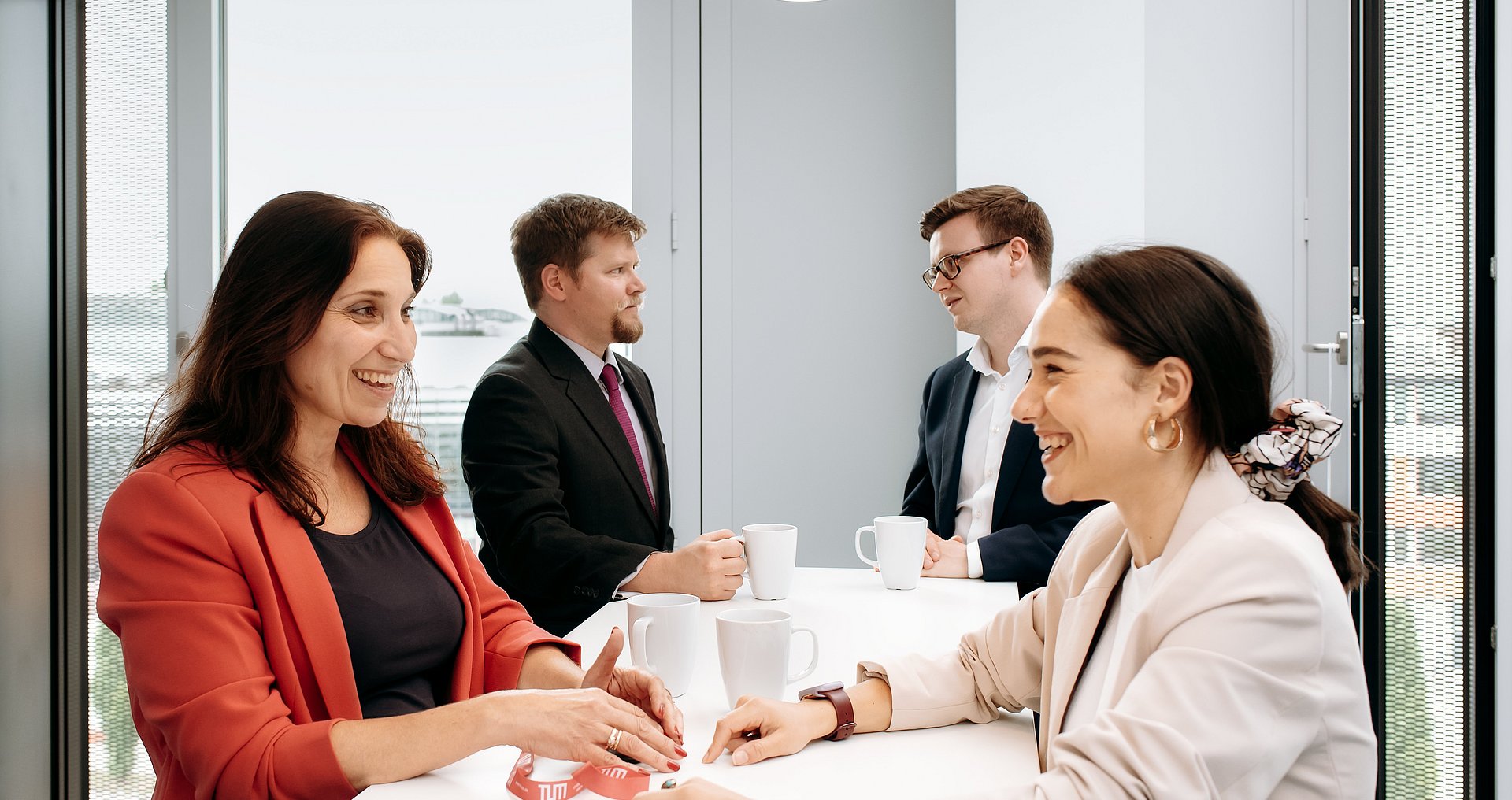 Two women and two men come together at a bar table and chat while drinking a cup of coffee.