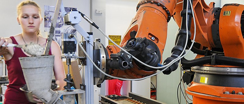 An der Versuchsanlage für additive Fertigung wird durch Extrusion von Holzleichtbeton ein multifunktionales Wandelement hergestellt. Bachelor-Studentin Bettina Saile befüllt den Versuchsextruder mit Frischbeton. (Foto: K. Henke / TUM) An der Versuchsanlage für additive Fertigung wird durch Extrusion von Holzleichtbeton ein multifunktionales Wandelement hergestellt. Bachelor-Studentin Bettina Saile befüllt den Versuchsextruder mit Frischbeton.