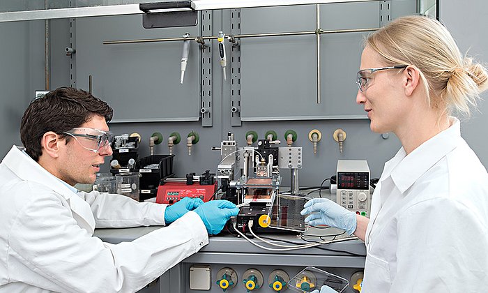 Stephan Pröller (li.) und Dr. Eva M. Herzig vor dem Drucker, mit dem Kunststoff-Solarzellen hergestellt werden.
