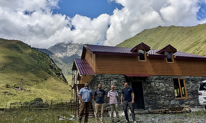 Four men are standing in front of a mountain ridge in the High Caucasus. 