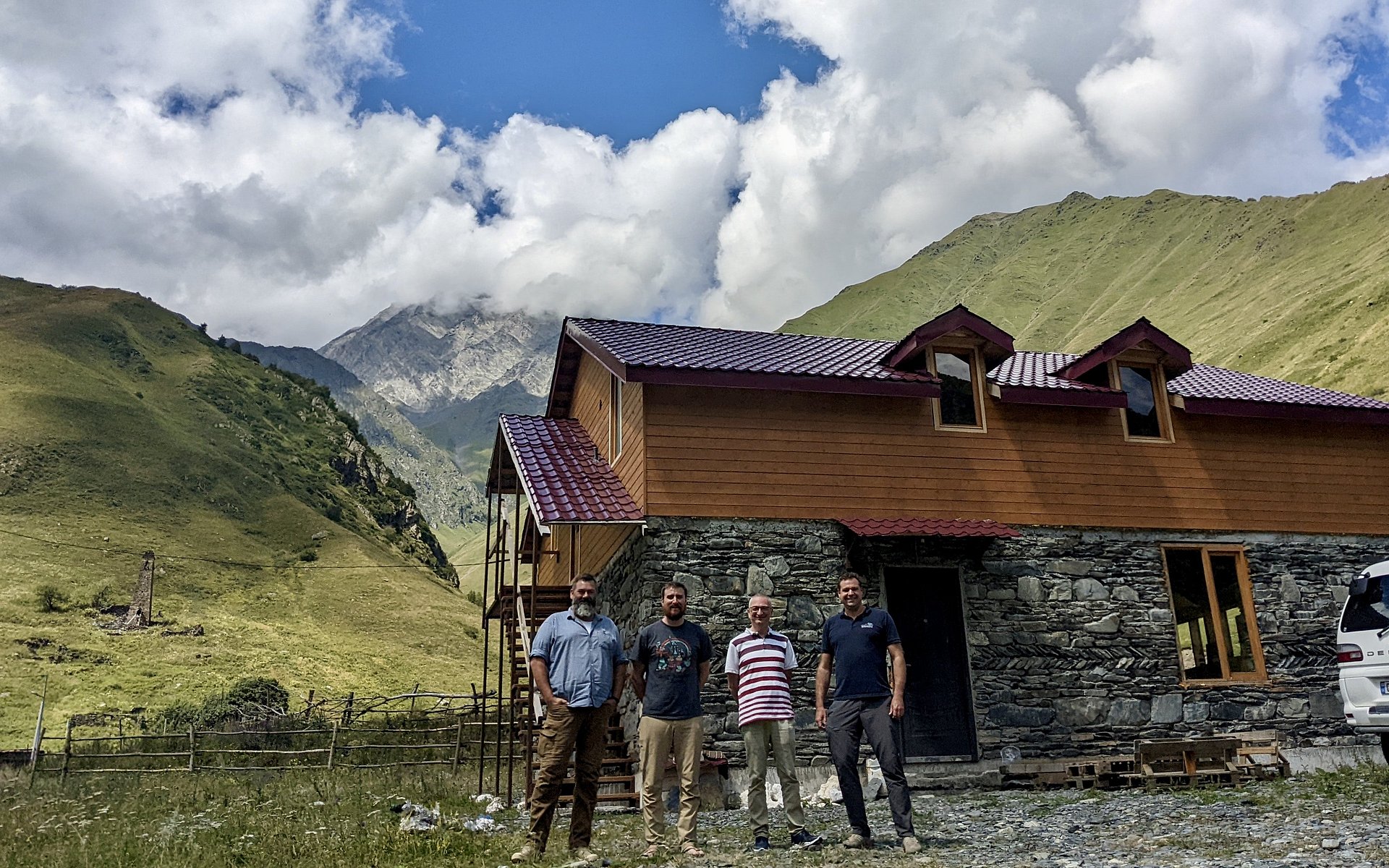 Four men are standing in front of a mountain ridge in the High Caucasus. 