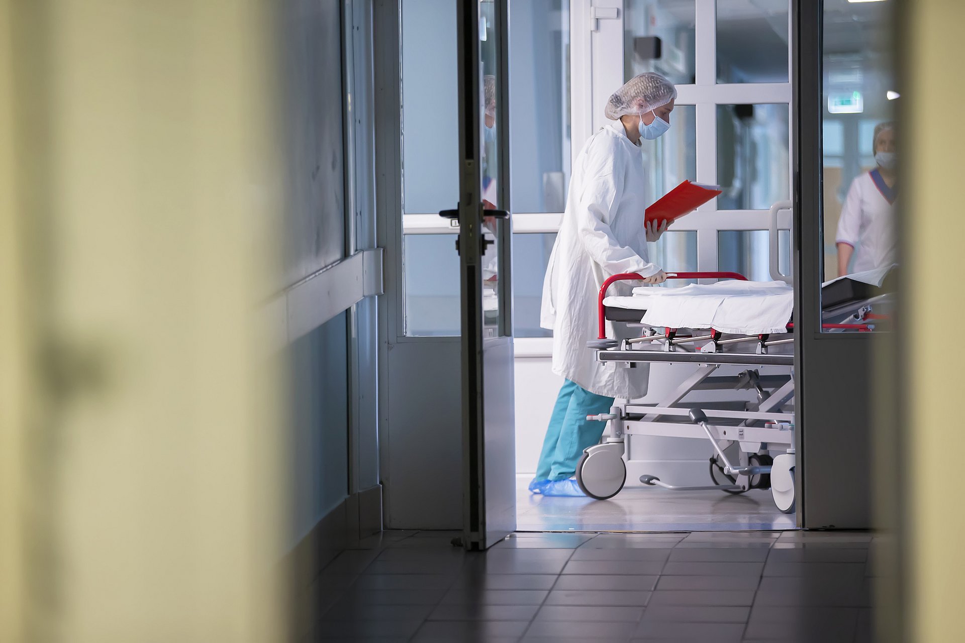 A hospital bed is pushed across a hospital corridor. A hospital bed is pushed across a hospital corridor.