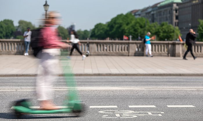 Ein Mensch fährt mit einem E-Scooter über eine Brücke