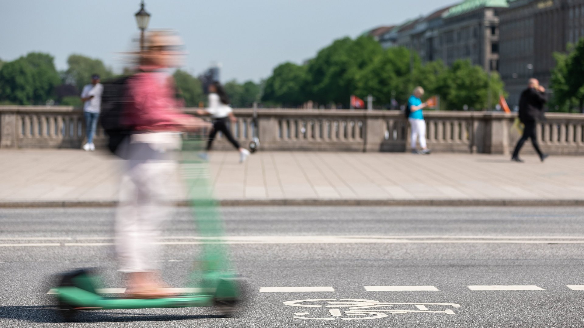 Ein Mensch fährt mit einem E-Scooter über eine Brücke Ein Mensch fährt mit einem E-Scooter über eine Brücke