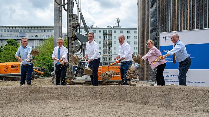 Die Rednerinnen und Redner setzen den ersten Spatenstich für das Gebäude.