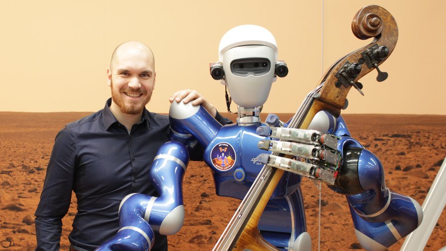 Adrian Bauer, a member of the TUM JazzBand, with the robot "Rollin' Justin". Only Bauer can play the double bass. (Photo: DLR CC-BY 3.0)