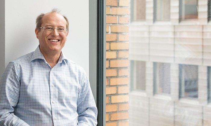 Prof. Gerhard Kramer steht lachend neben einem Fenster.
