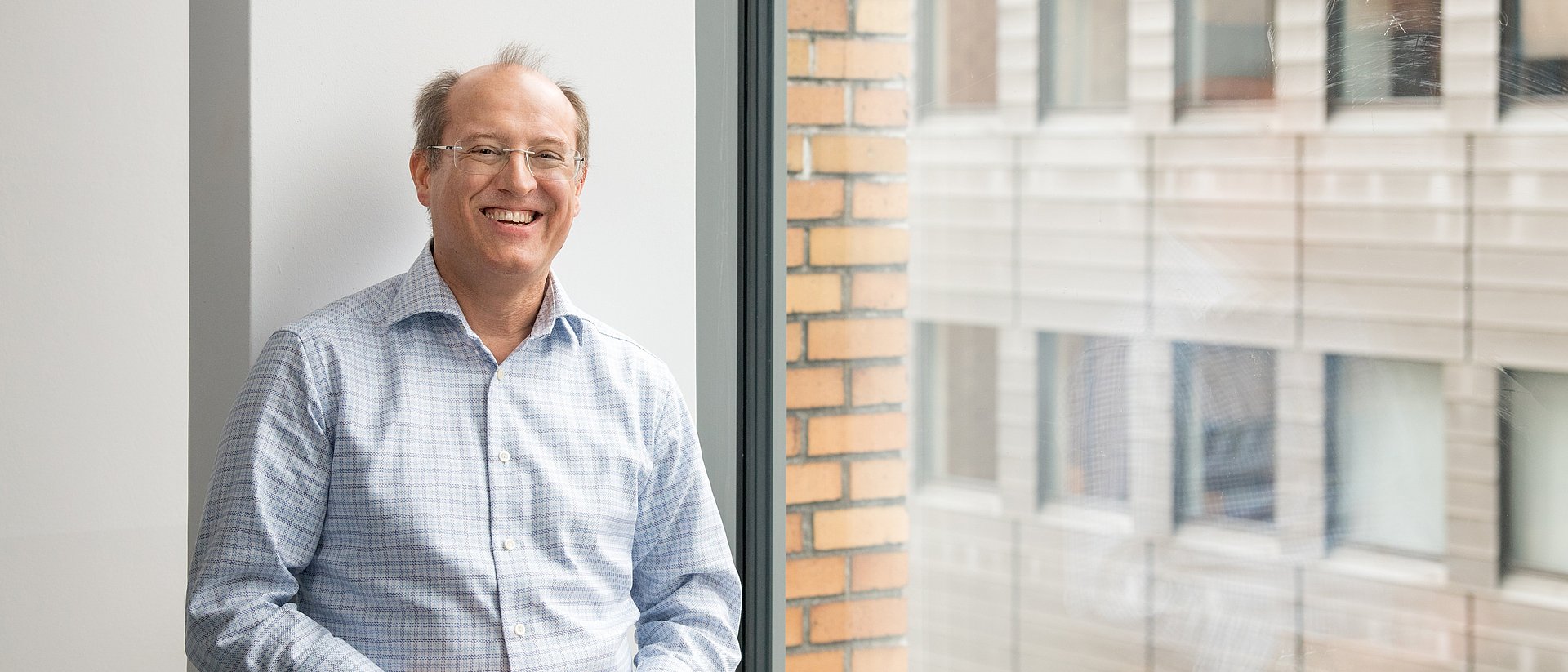 Prof. Gerhard Kramer steht lachend neben einem Fenster.