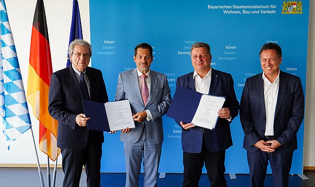 Vier Männer aus Wissenschaft, Industrie und Politik stehen vor einer Fotowand.