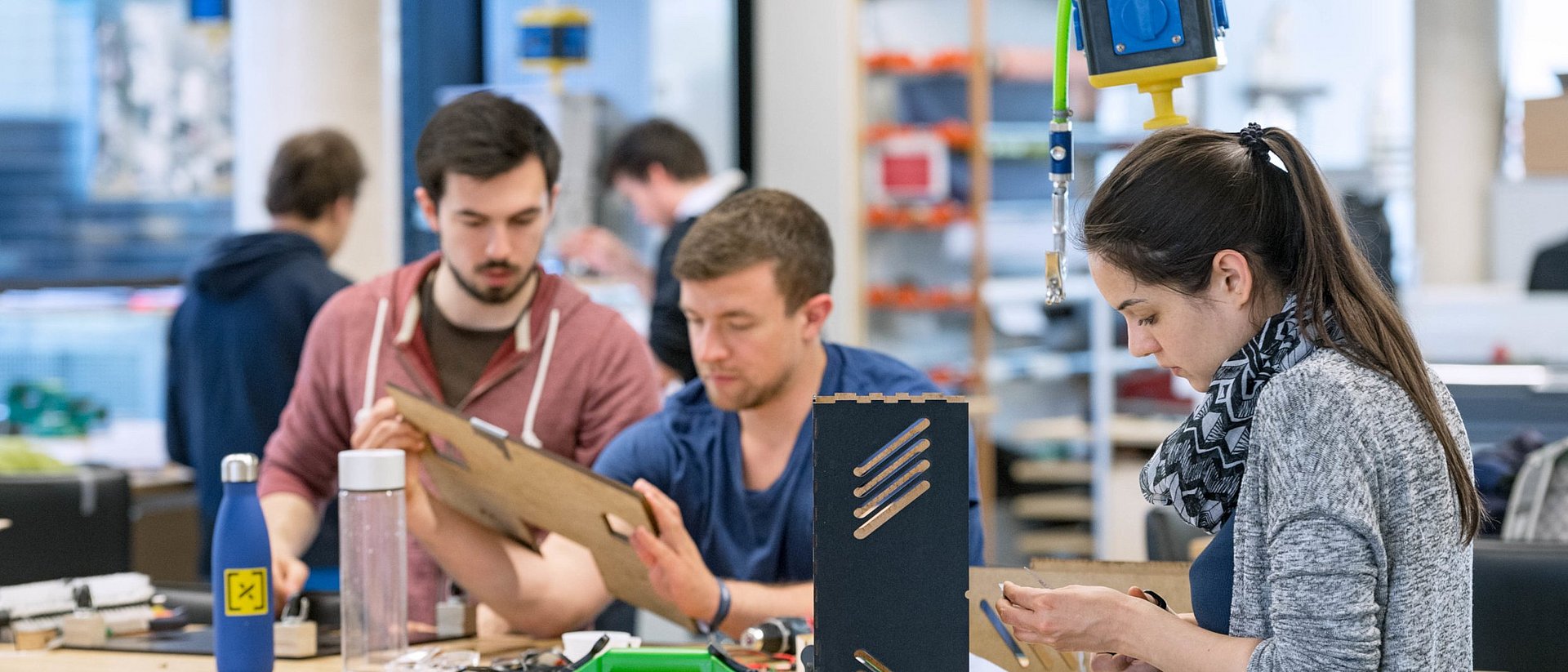 Two male and one female student work together on a model at a table in a workshop.