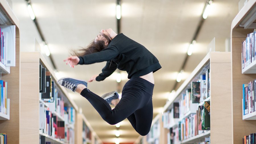 Woman jumping in front of bookshelf