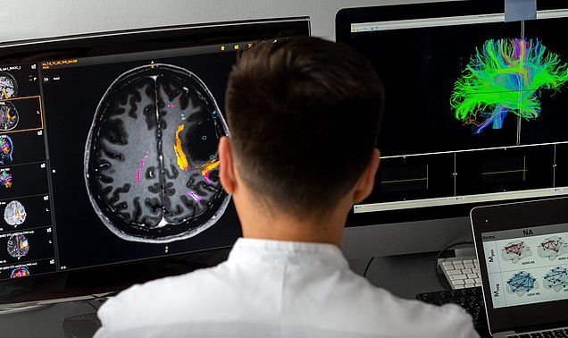 Forscher sitzt vor zwei Bildschirmen und macht eine 