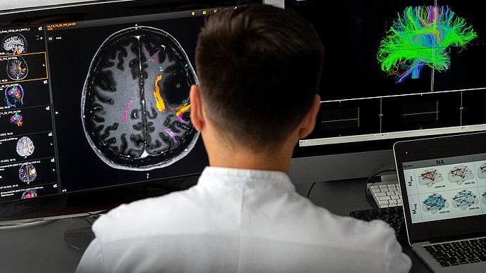 Forscher sitzt vor zwei Bildschirmen und macht eine 