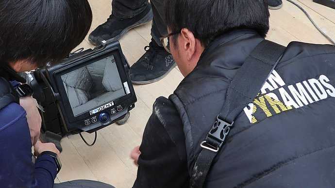 Nachweis einer neuen Kammer in der Cheops-Pyramide von Gizeh Researchers stand around the screen of an endoscope.