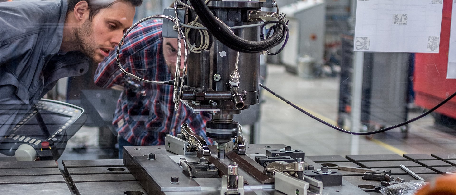 Dr. Andreas Bachmann (li.) beobachtet durch ein Sicherheitsglas, wie der Roboter zwei Metallplatten mit dem schnell drehenden Schweißstift zusammenschweißt.