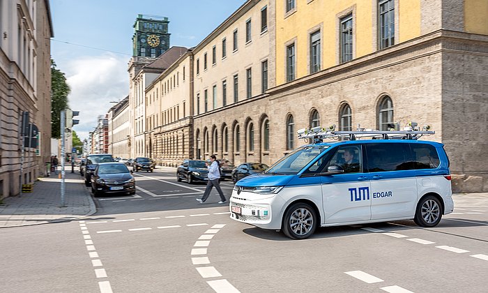 Ein Kleinbus mit Dachaufbau und Sensorik zur Erprobung des Autonomen Fahrens fährt an der Universität vorbei.