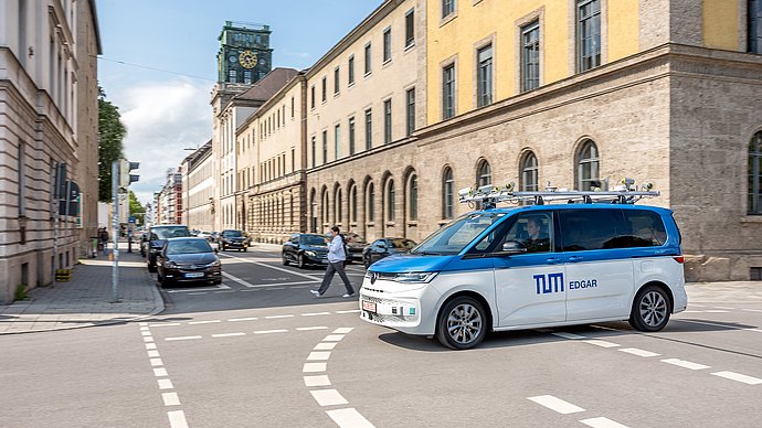 Ein Kleinbus mit Dachaufbau und Sensorik zur Erprobung des Autonomen Fahrens fährt an der Universität vorbei.