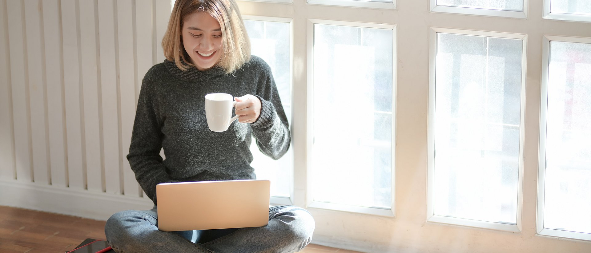 Frau mit Laptop und Kaffeetasse in ihrer Wohnung