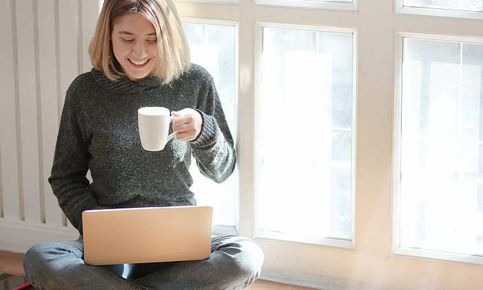 Frau mit Laptop und Kaffeetasse in ihrer Wohnung