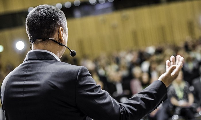 Man speaks in front of an audience with a headset