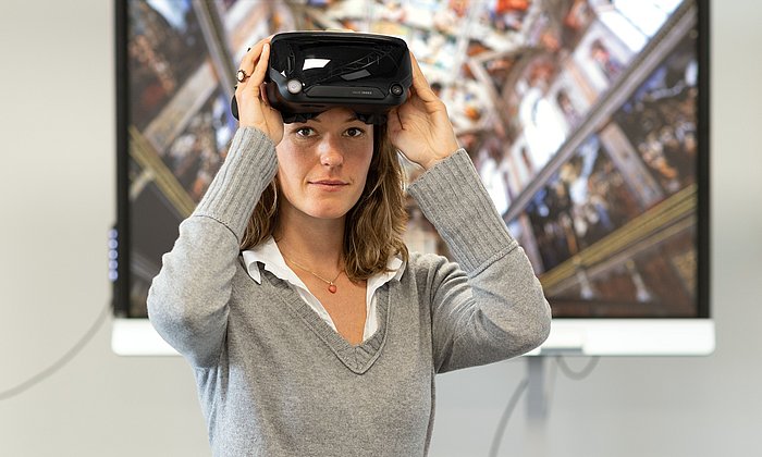 Eine Frau mit einer VR-Brille steht vor einem Bildschirm. 