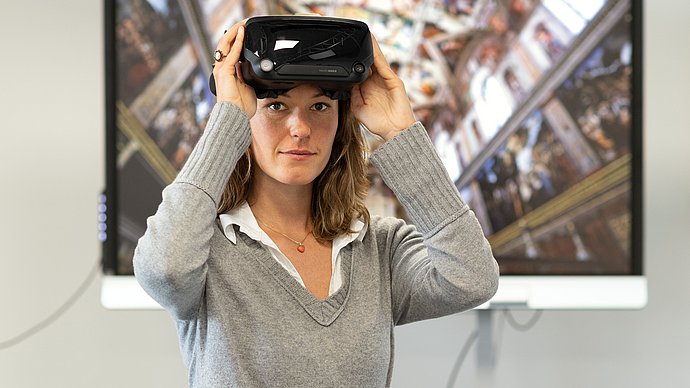 Eine Frau mit einer VR-Brille steht vor einem Bildschirm. 