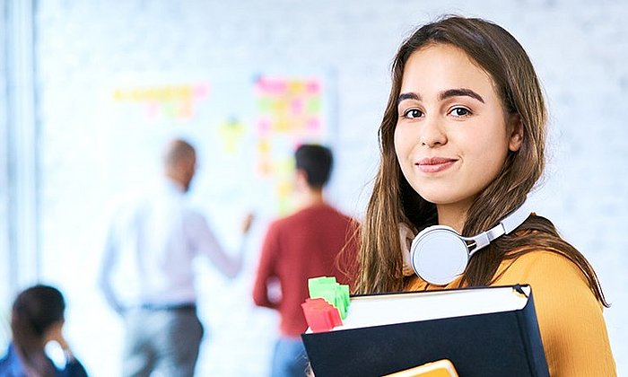 Female student looking into the camera, in the background a bright, modern seminar room