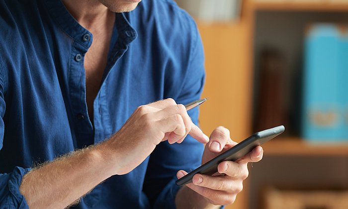 A man holds a cell phone in his hand, which he is currently operating.