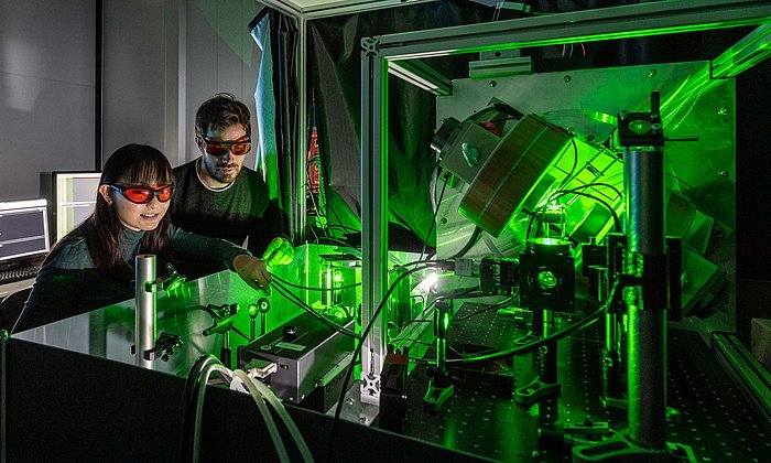 Zwei junge Forschende, eine Frau und ein Mann, richten den Laser für ein Quantensensorexperiment aus