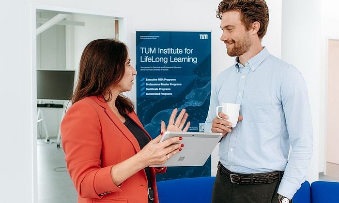 Mann und Frau in Businesskleidung im Gespräch vor einem Roll-up des TUM Institute for LifeLong Learning