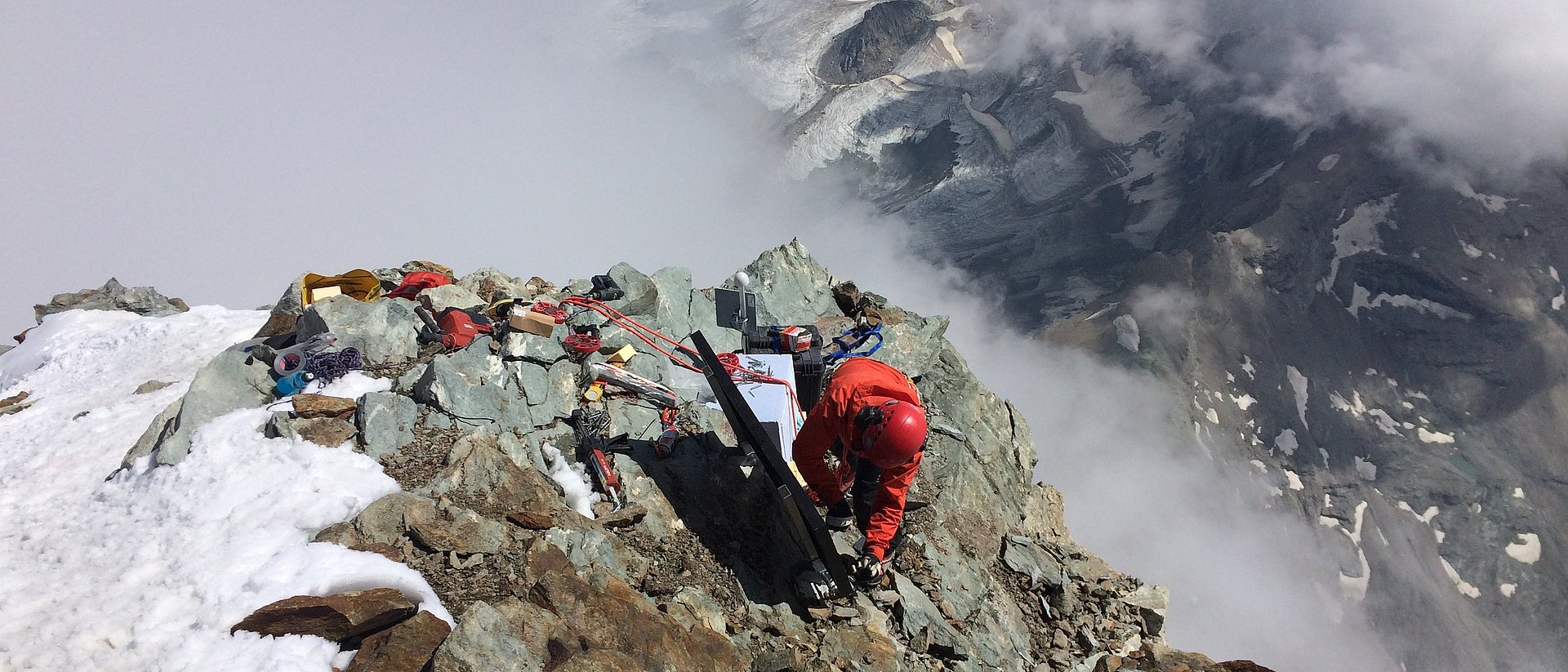 A man works on a mountain top partially covered with snow.