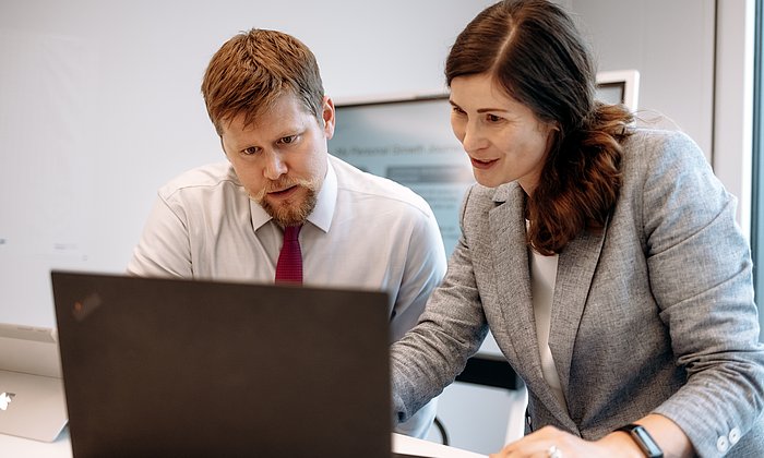 Ein Mann und eine Frau stehen vor einem Laptop und nehmen an einem virtuellen Kurzimpuls teil.