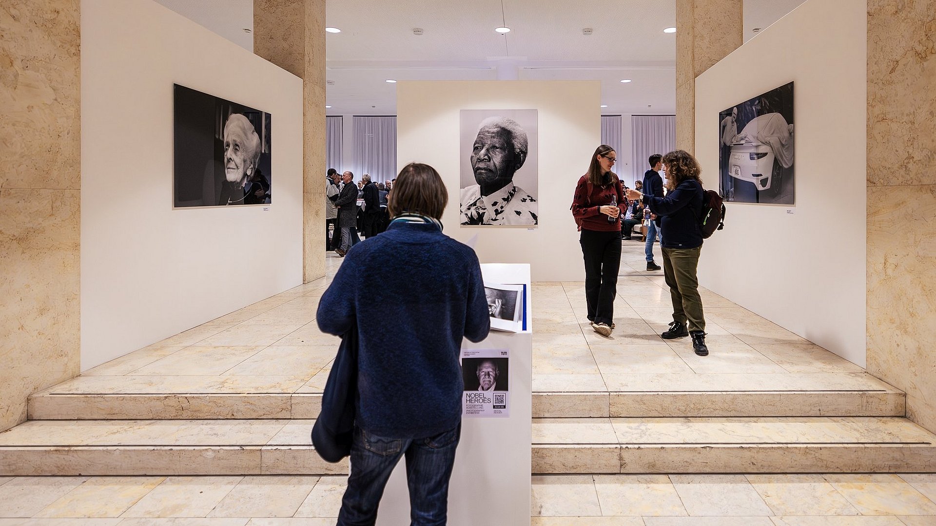 Gäste der Foto-Ausstellung "Nobel Heroes" sehen sich die Fotografien von Peter Badge in der Immatrikulationshalle der TUM an. 