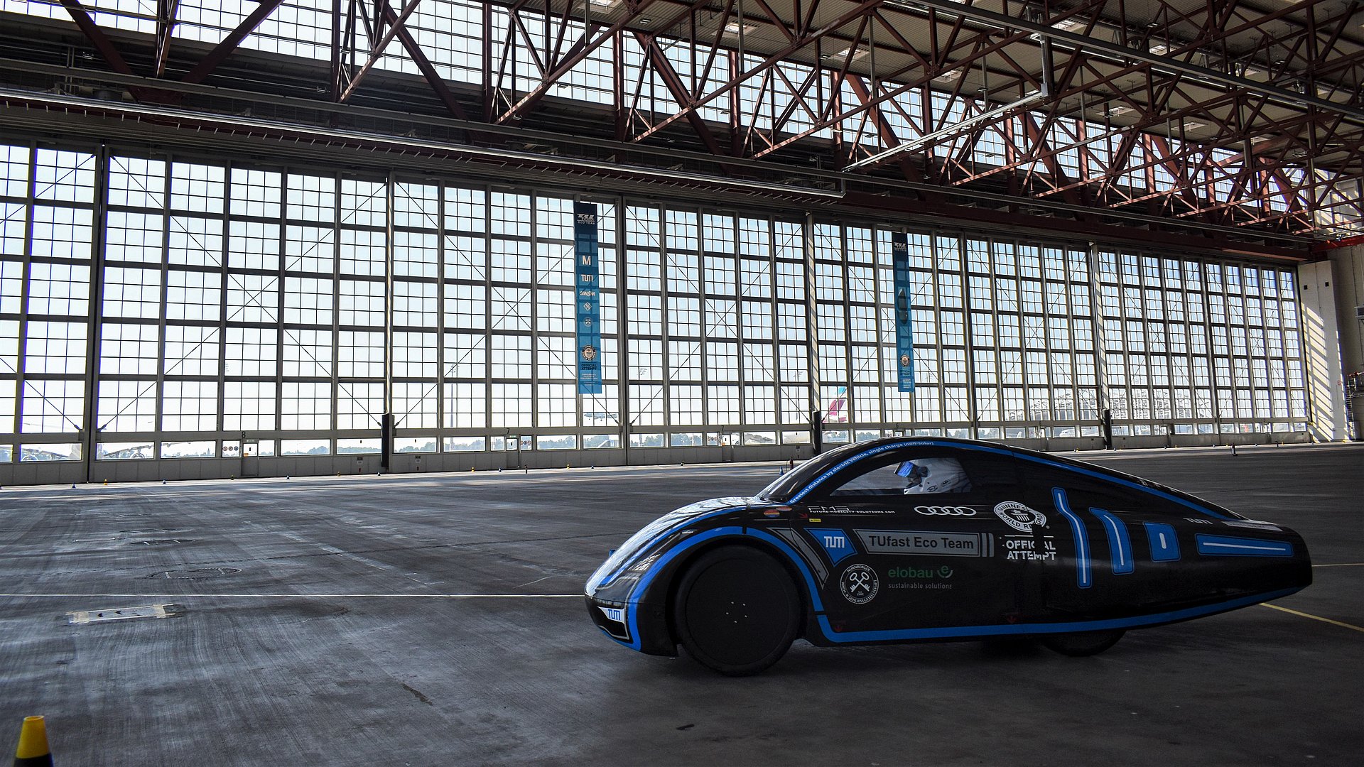 A competition car drives in an airplane hangar to break a world record.