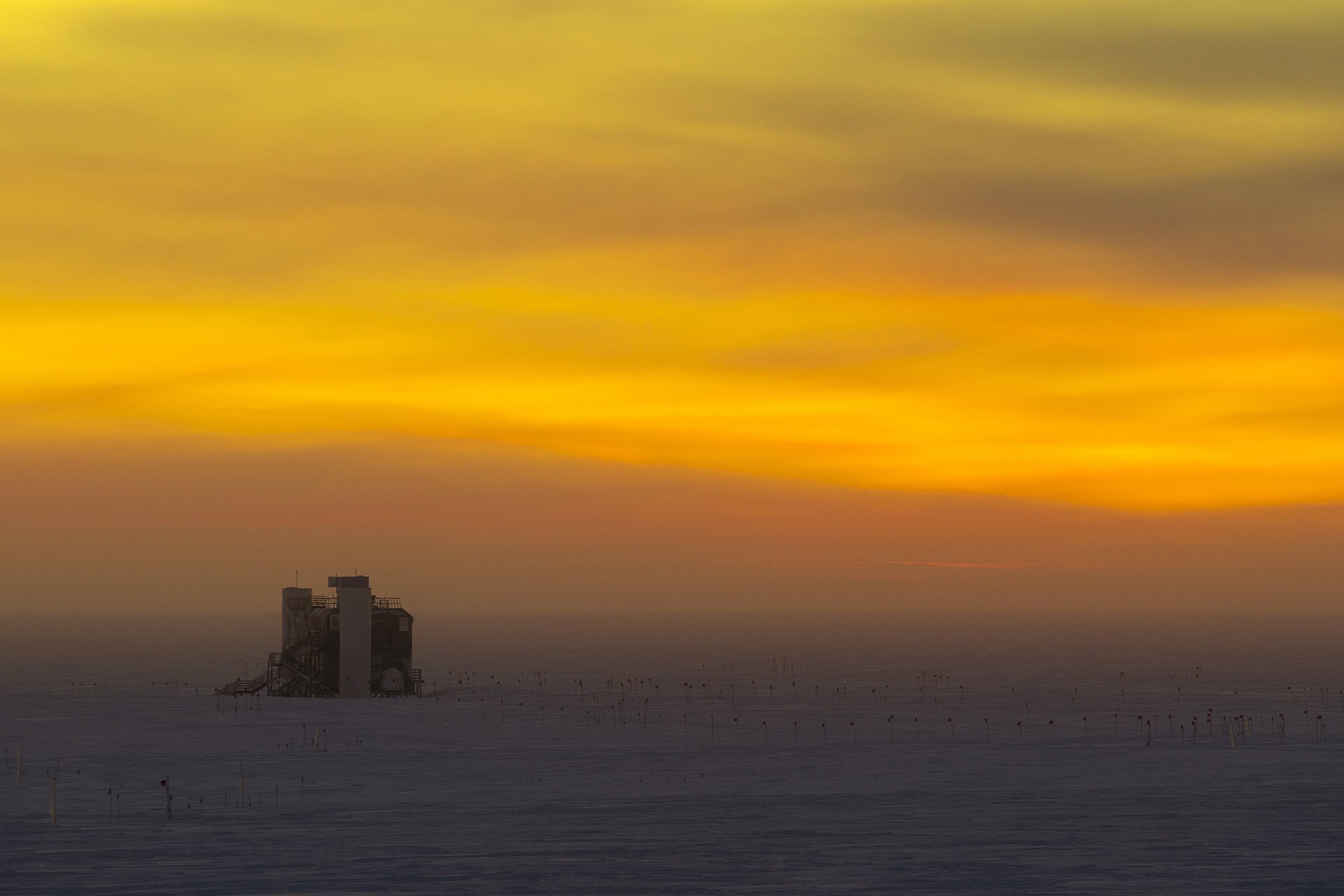 The IceCube laboratory in the distance against the sky colored orange by the sunset.