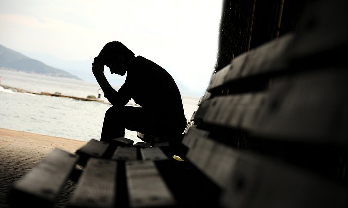 A man sitting on bench holding his head.