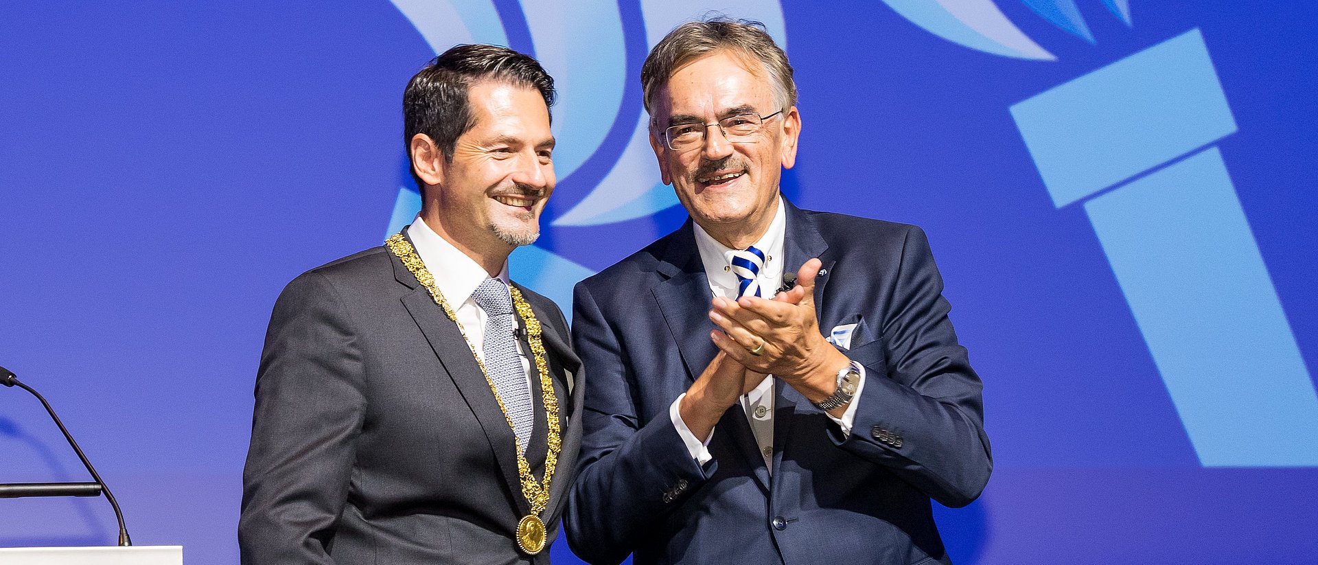 Wolfgang A. Herrmann und Thomas F. Hofmann auf der Bühne des Audimax der TUM. Hofmann trägt die Amtskette.