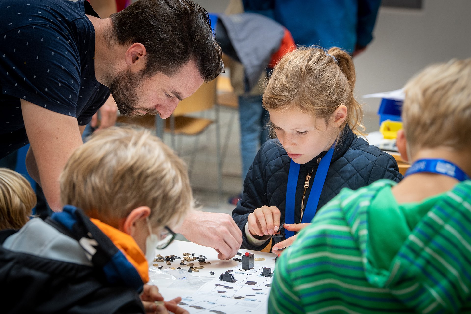 A man builds a Lego model at a table with other children.
