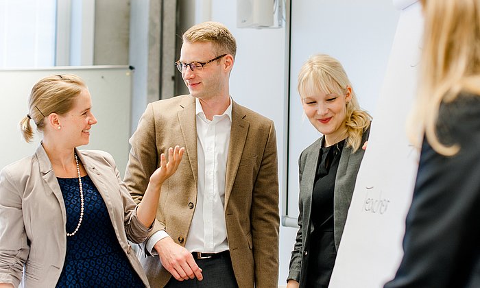 Three women and a man stand in front of a flipchart and discuss it.