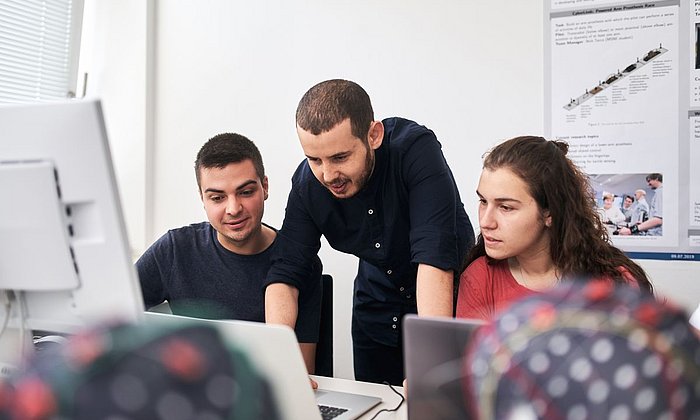 Students exchange ideas about a subject together in front of a screen.