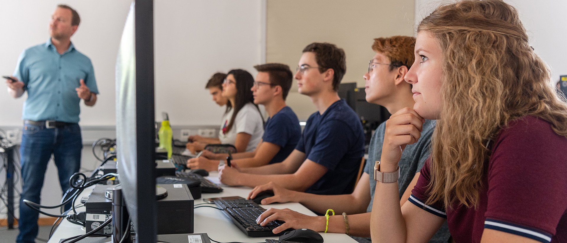 Studierende Ein Dozent und Studierende an Computern.