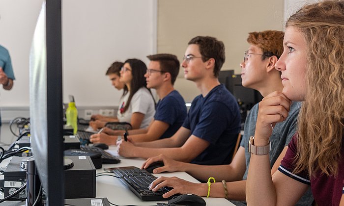 Ein Dozent und Studierende an Computern.