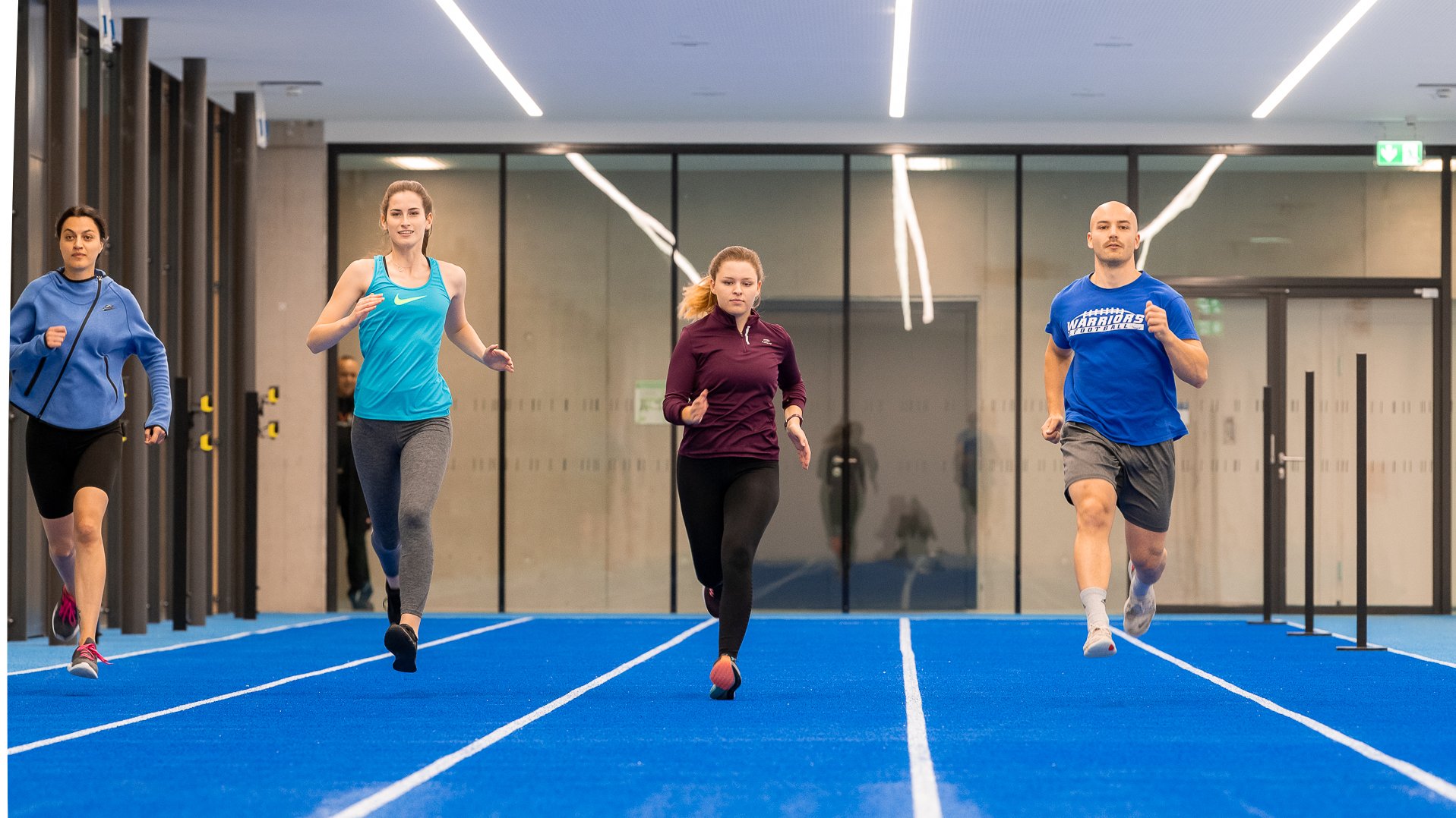 Studierende sprinten in einer neuen Sporthallen. Vier Stueirende sprinten in einer der größten neuen Sporthallen.