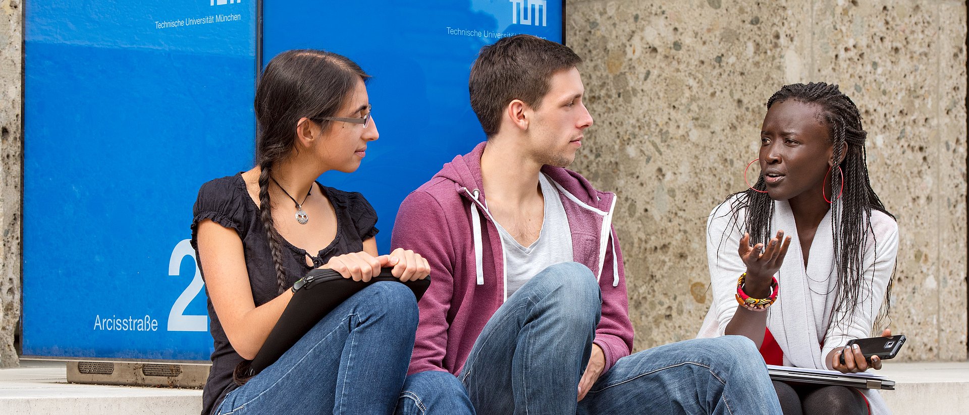 Students sitting on the stairs of the main entrance to the TUM.